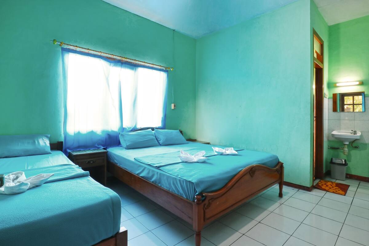A room with two beds, a window with curtains, a bedside table, a nightstand, a sink, and a tiled floor.