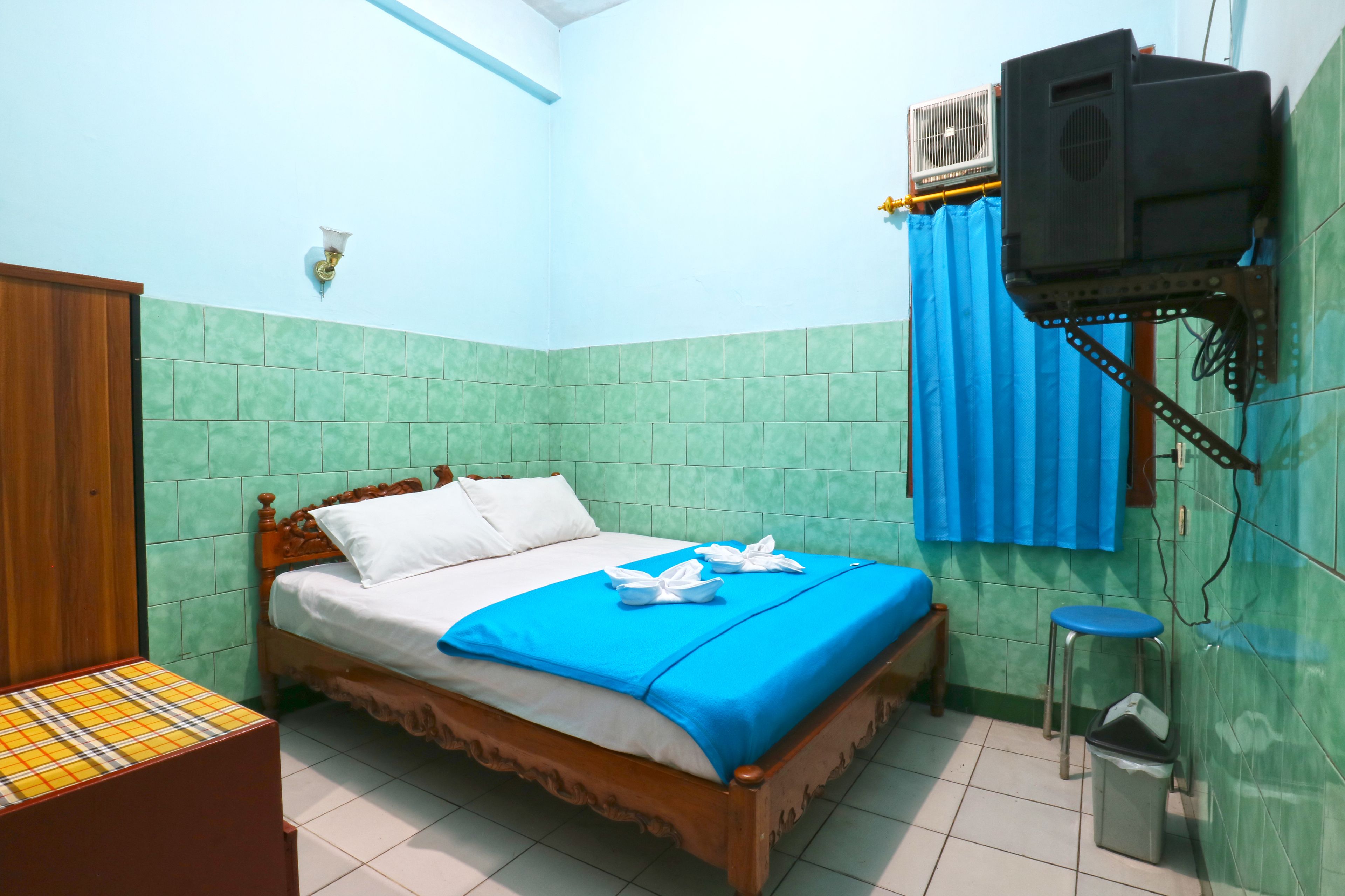 A room with a wooden bed, a blue curtain, a wall-mounted air conditioner, and a small stool.