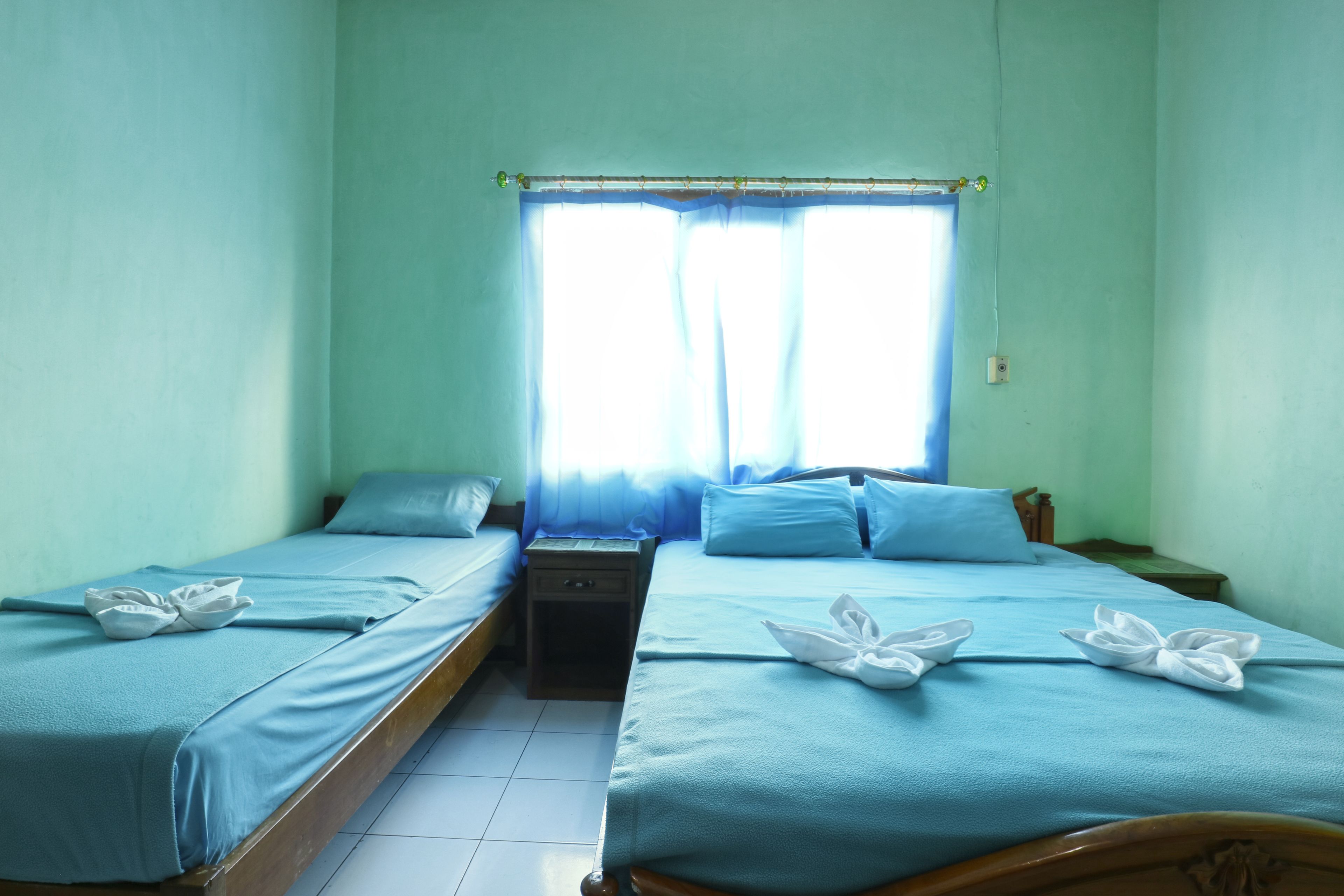 A twin room with two beds, a nightstand, and a window with curtains.