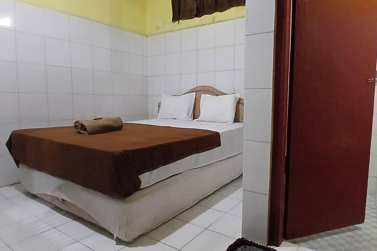 Una habitación de hotel con una cama, una manta marrón y un colchón blanco.