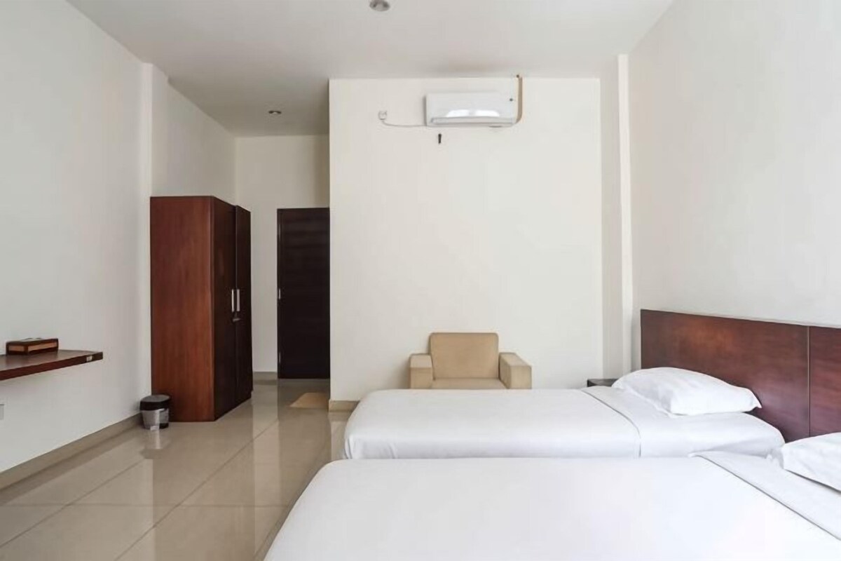A hotel room with two beds, a wooden wardrobe, a chair, and a small table.