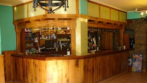 A wooden bar area with shelves stocked with various bottles and snacks, a television, and a Nestle advertisement. - Hotel Rural Huelde (Cremenes)