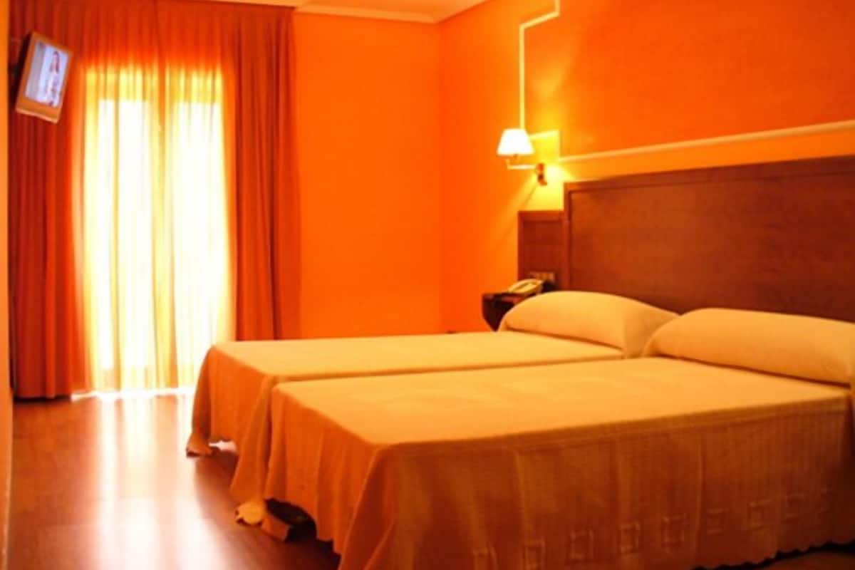 Quarto de hotel com duas camas, televisão e mesa de cabeceira.