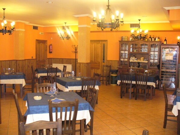 Un restaurante con varias mesas y sillas, una estantería para vinos y un candelabro.