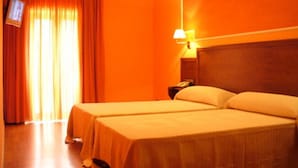 A hotel room with two beds, a television, and a nightstand with a lamp. - Hotel Rural Huelde (Cremenes)