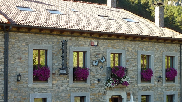 A stone building with multiple windows, some with flower boxes, and a sign indicating a restaurant. - Hotel Rural Huelde (Cremenes)