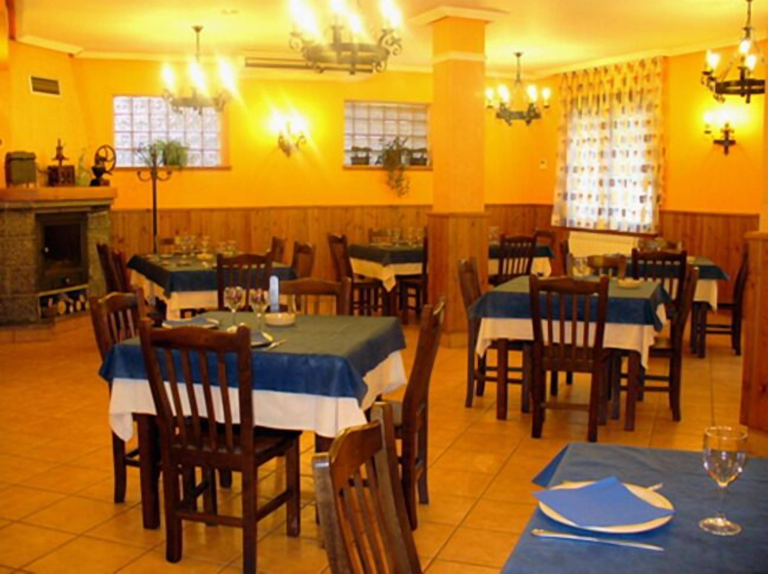 A dining area with tables set for two, wooden chairs, and a fireplace.