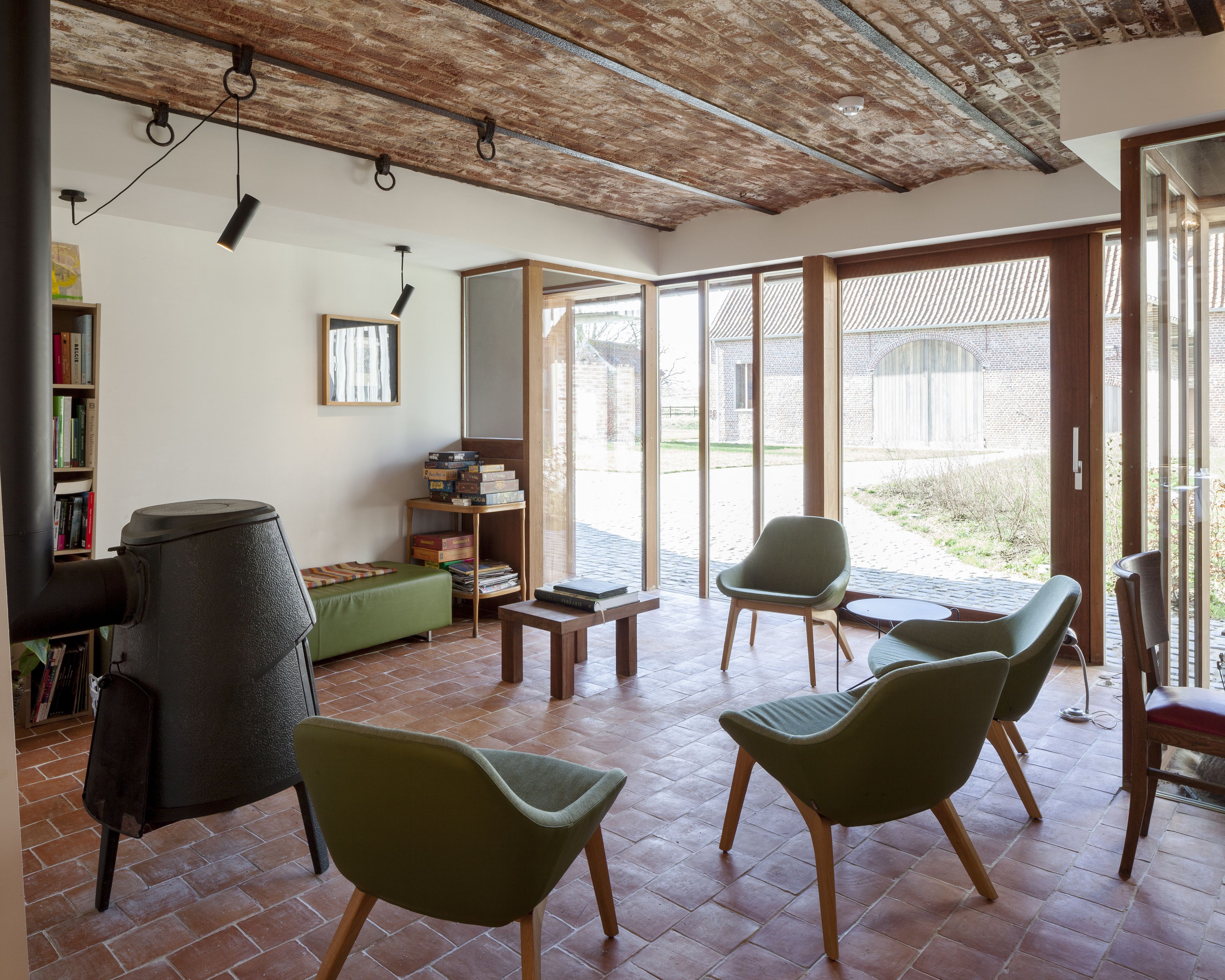 A spacious living area with a fireplace, green chairs, a wooden table, and a bookshelf.