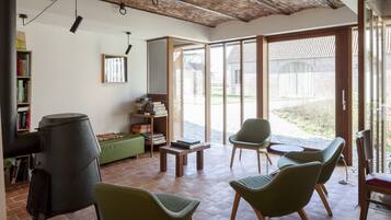 A spacious living area with a fireplace, green chairs, a wooden table, and a bookshelf.