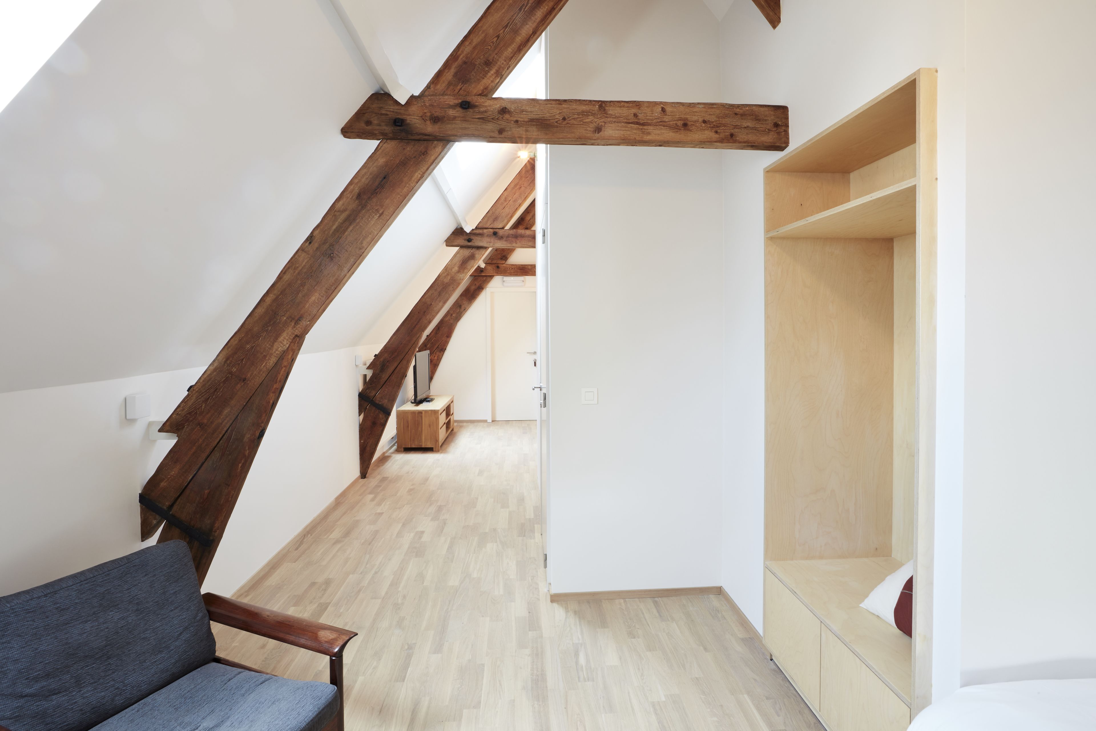 Une pièce avec un plafond en pente, des poutres en bois, un canapé, un banc en bois et un mur blanc.