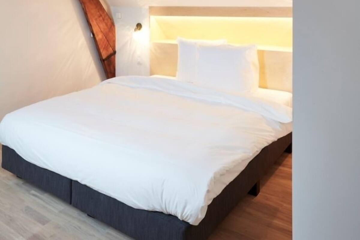 Een slaapkamer met een schuine hemel, een bed en een hanglamp.