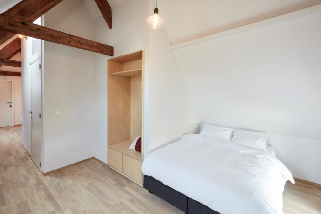 A bedroom with a large bed, built-in wooden shelving, and a slanted ceiling.