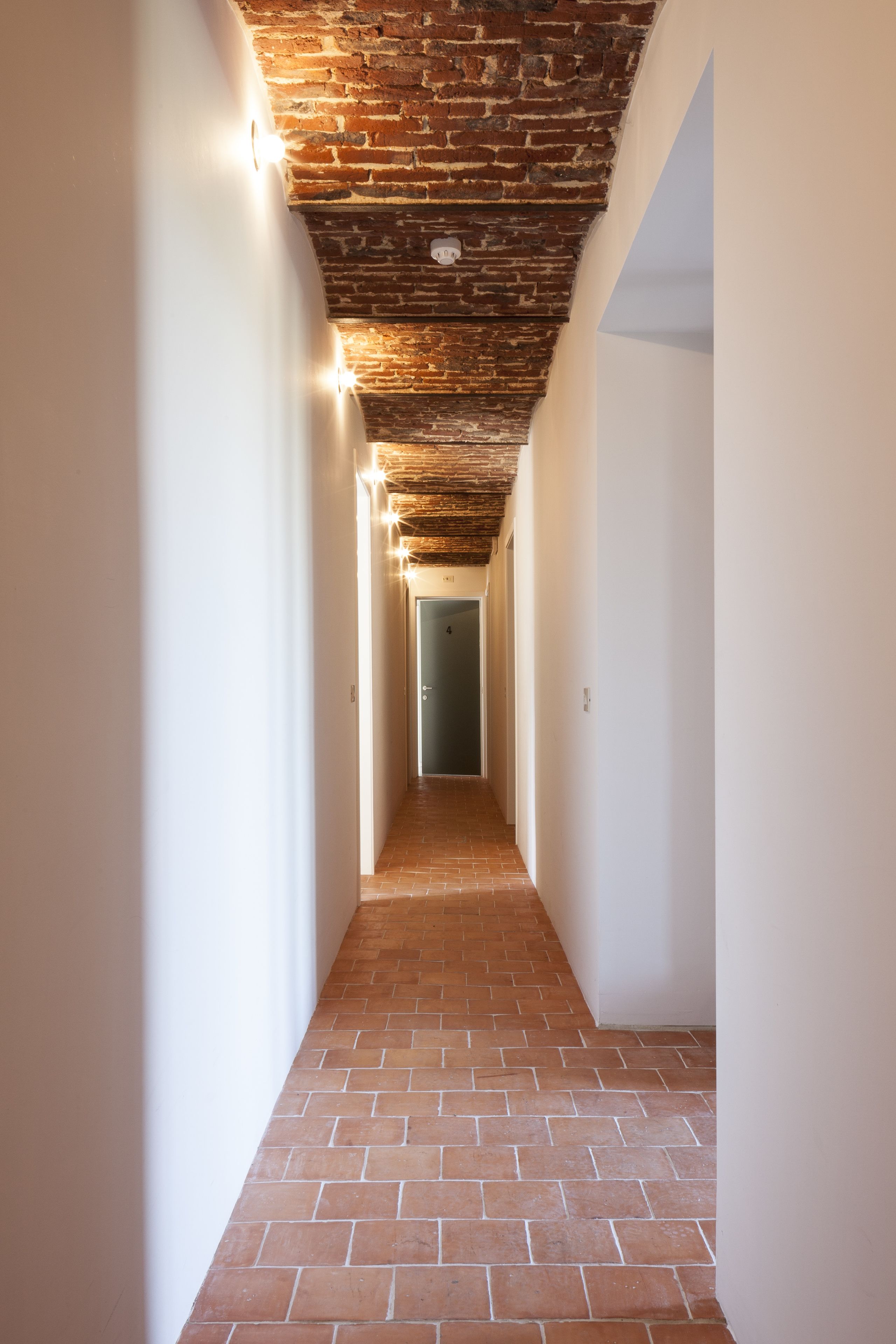 Un couloir doté d’un sol en briques et d’un plafond laissant apparaître les briques, qui mène à une porte.