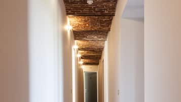 Un couloir doté d’un sol en briques et d’un plafond laissant apparaître les briques, qui mène à une porte.