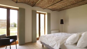 Ein Schlafzimmer mit einem großen Bett, einem Sessel und einer Heizung. Zwei Türen führen zu einem Außenbereich.