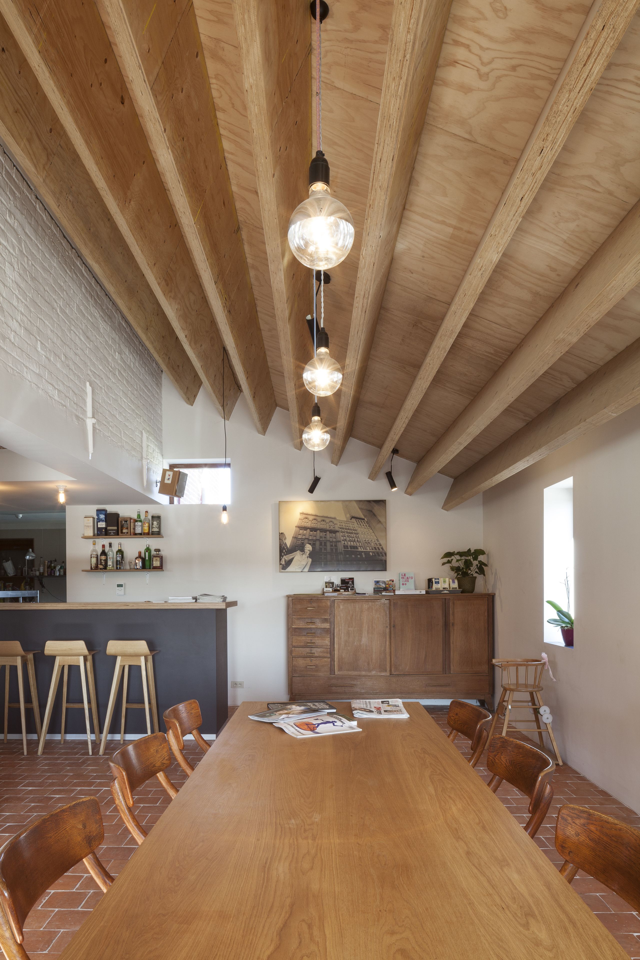 A spacious dining area with a long wooden table, several wooden chairs, and hanging pendant lights.