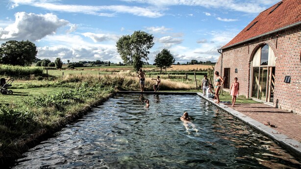 Ein Schwimmbecken neben einem Backsteinhaus unter blauem Himmel.