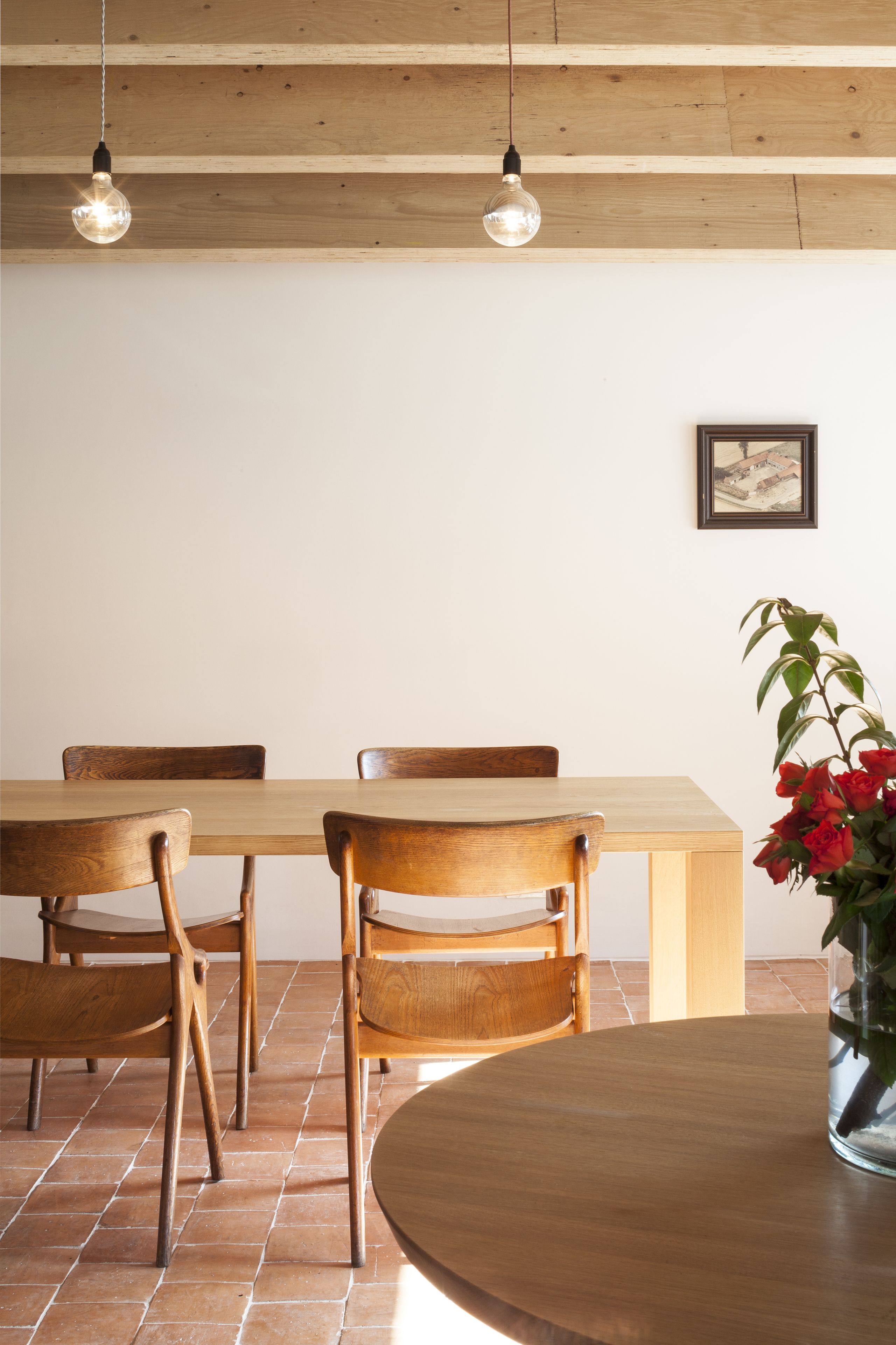 Un área de comedor con una mesa y sillas de madera, un florero con flores y una bombilla colgante.