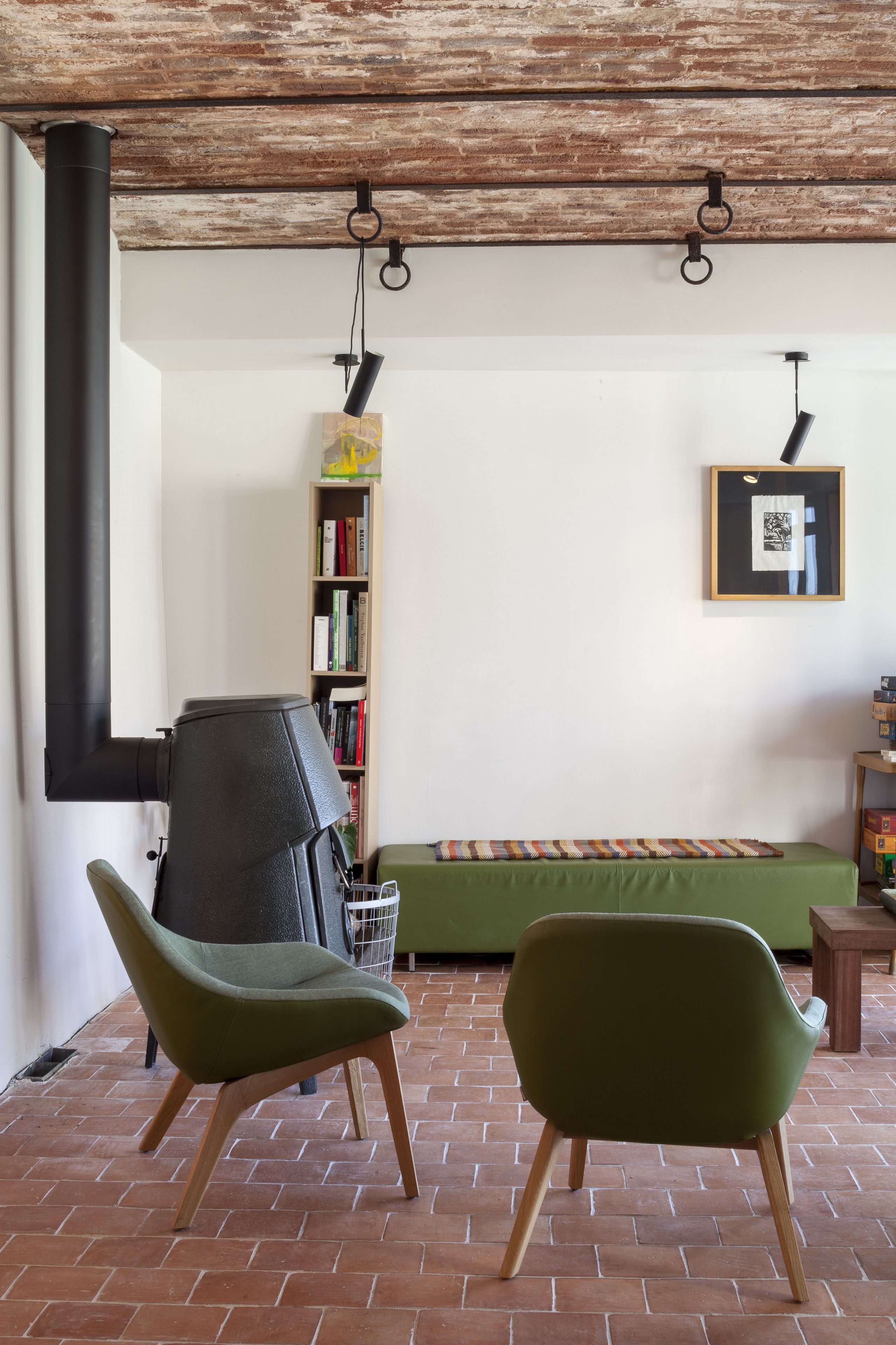 Een kamer met een tegelvloer, een groene bank, een boekenkast en een ingelijst schilderij aan de muur.