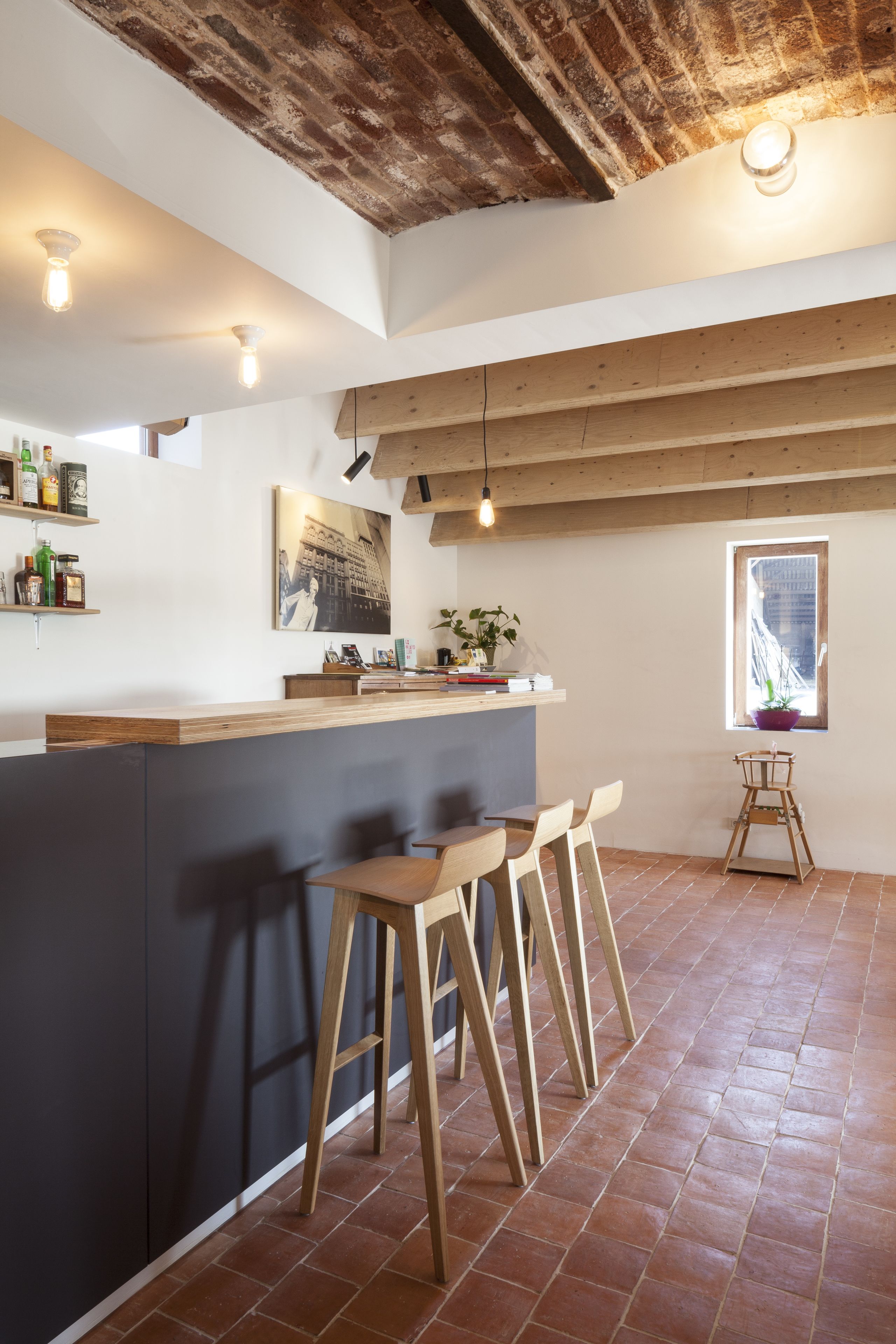 Une cuisine dotée d’un îlot central, de tabourets en bois, d’un plafond en briques et d’une fenêtre offrant une vue dégagée.
