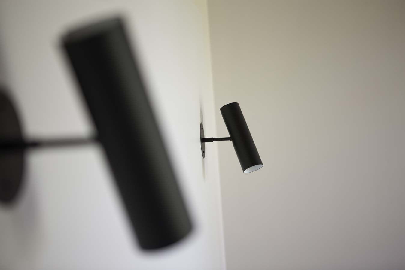 A modern wall-mounted light fixture with a cylindrical shade.