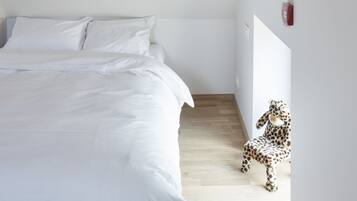 Een slaapkamer met een bed, een fauteuil met luipaardprint en een witte muur met een lichtschakelaar.