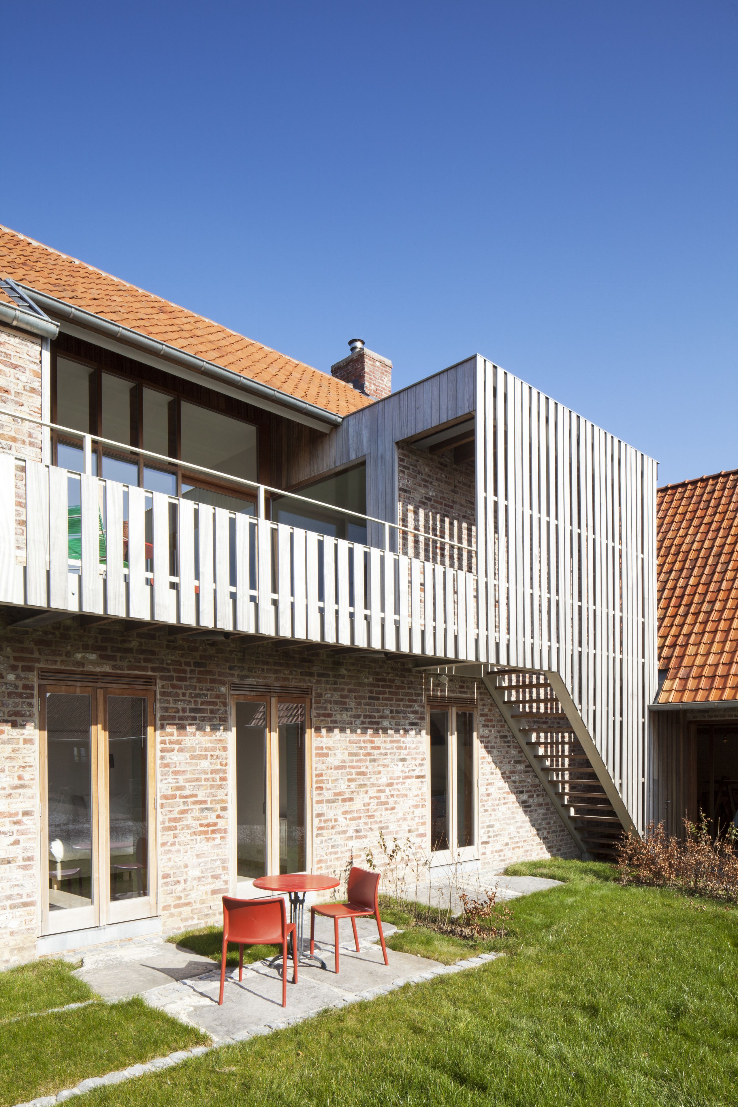 Een modern herenhuis met twee verdiepingen, een bakstenen gevel, grote ramen en een balkon.