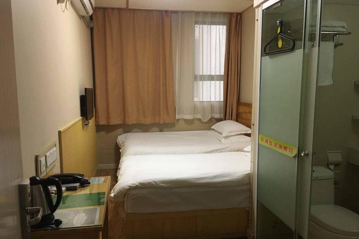 A hotel room with two beds, a wooden desk with a telephone, a glass shower enclosure, and a toilet.