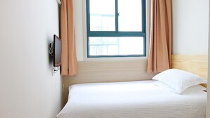 Un lit simple avec une literie blanche, dans une pièce dotée d’une fenêtre et de rideaux.