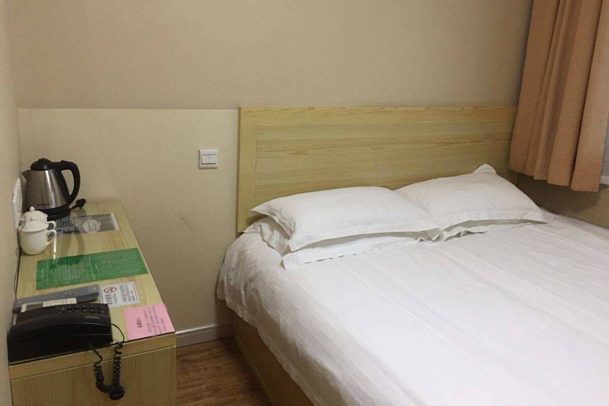 A hotel room with a bed, a wooden nightstand, a kettle, a telephone, and a small table with a menu.