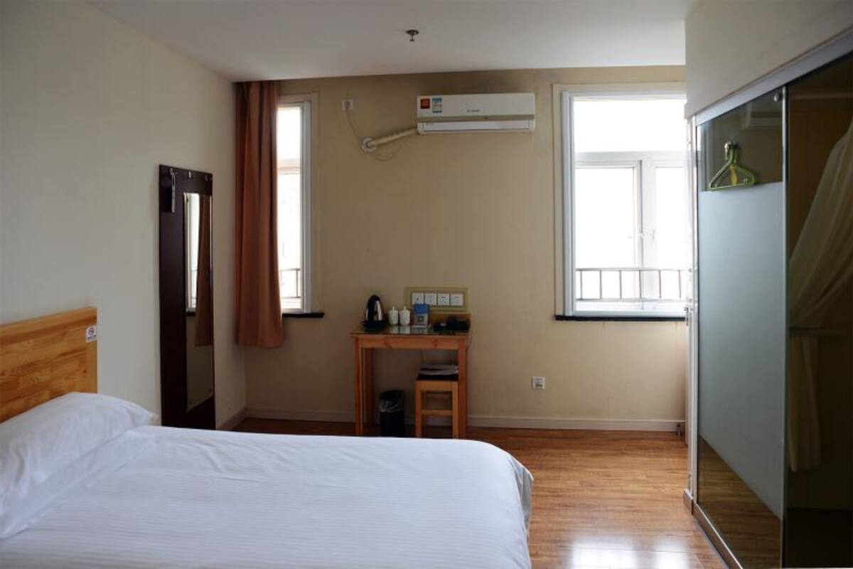 A hotel room with a bed, a desk with a chair, an air conditioning unit, and a wardrobe.