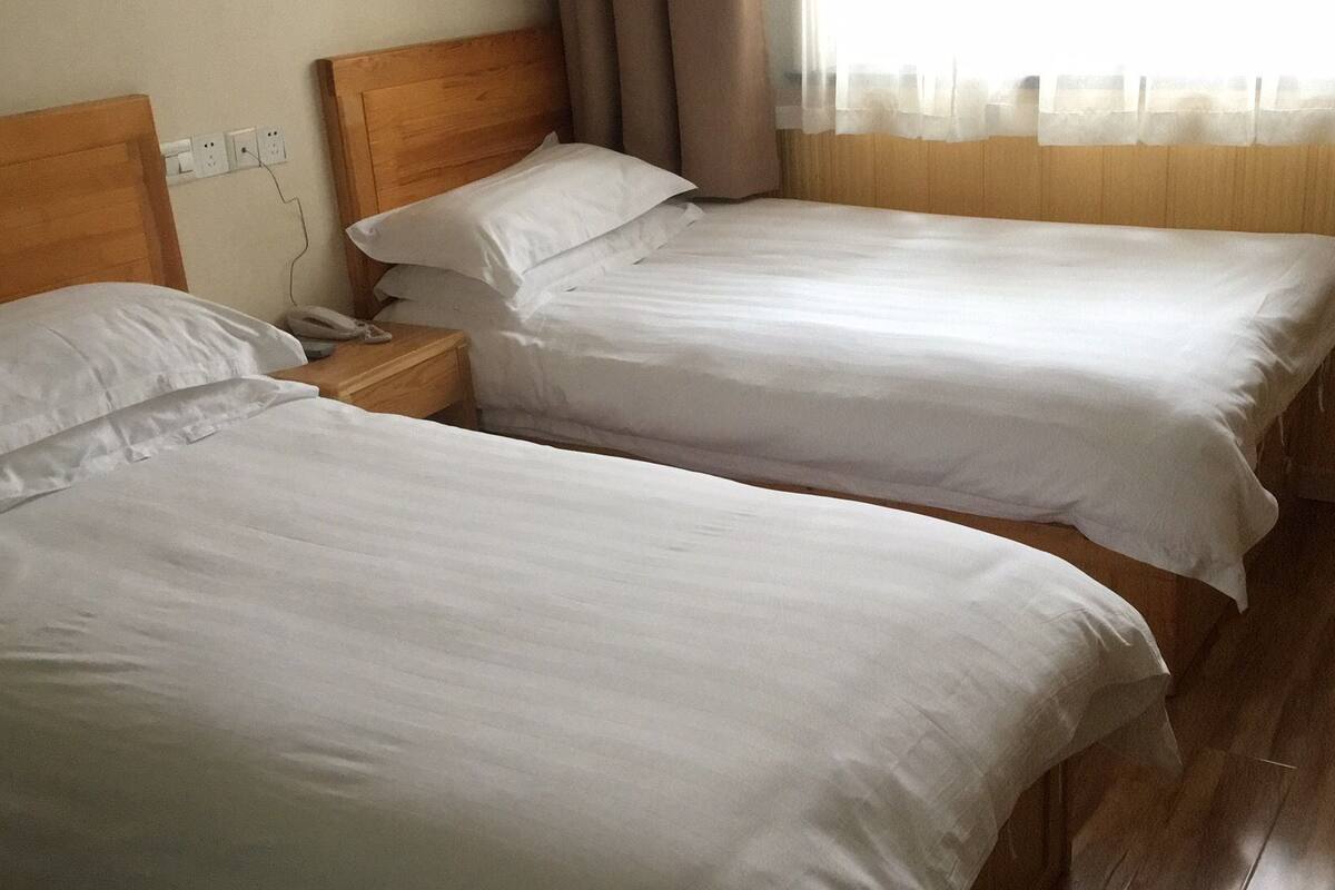 Two single beds with wooden headboards in a room with wooden flooring and a window with sheer curtains.