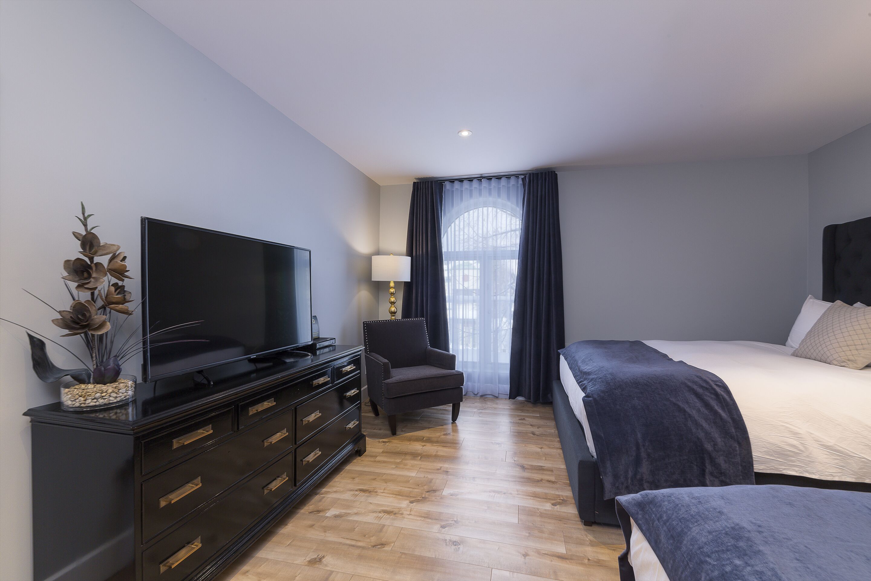 A modern bedroom with a large bed, a TV on a black dresser, and a chair.