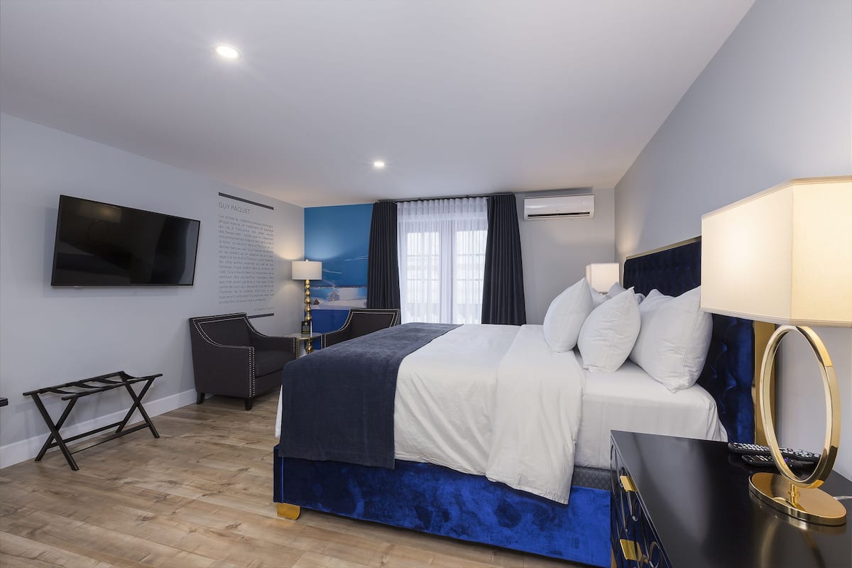 A hotel room with a bed, bedside table, lamp, and a TV mounted on the wall.