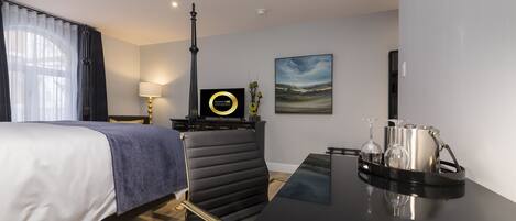 Une chambre d’hôtel moderne avec un lit, un bureau sur lequel se trouve un plateau avec des verres, une lampe, un tableau au mur et une fenêtre avec des rideaux.