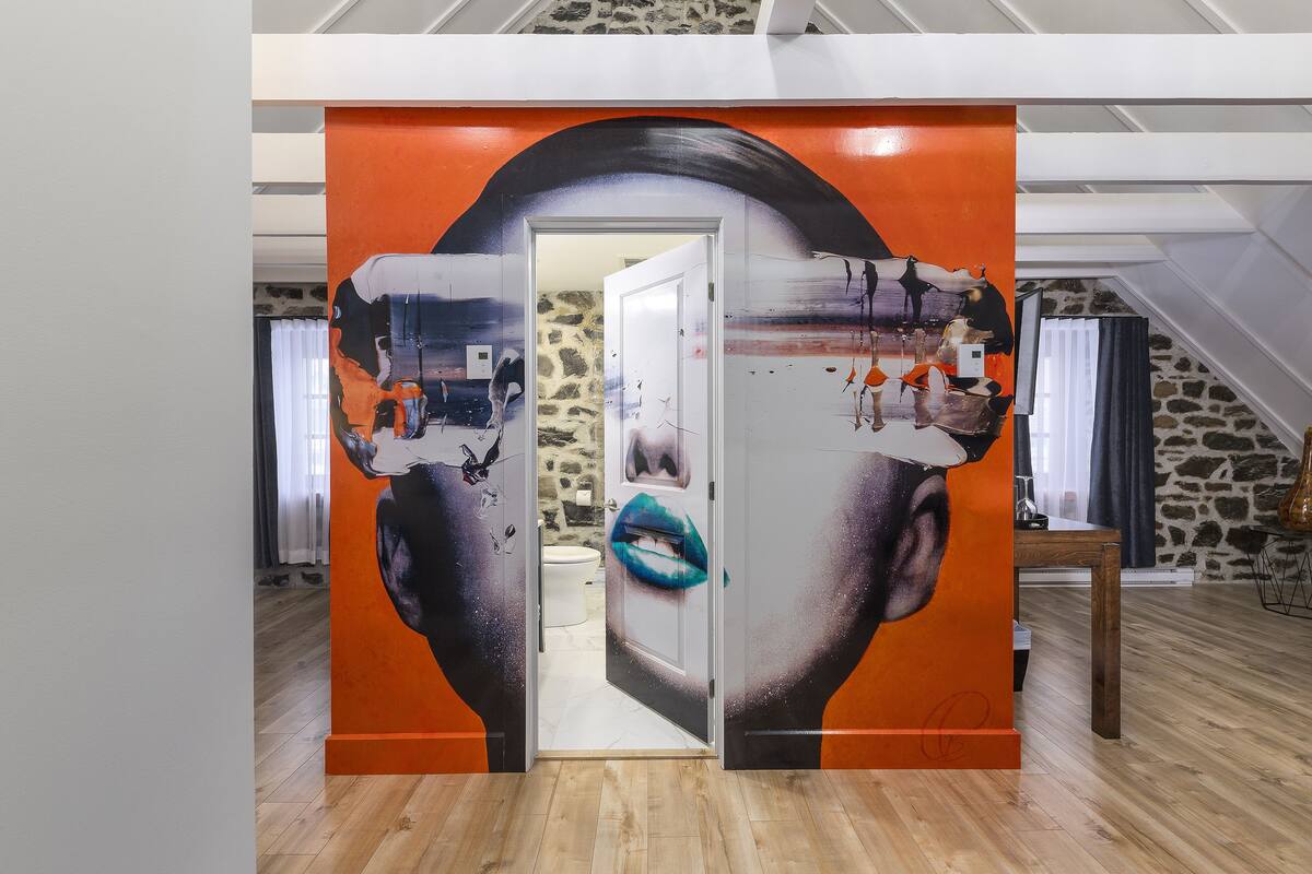 A room with a large mural on the wall, a wooden floor, and a stone wall in the background.