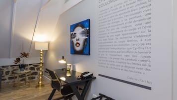 Un espai d'oficina modern amb escriptori, cadira, làmpada i un mural amb una obra d'art i text.