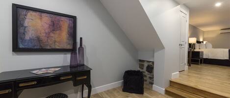 Une chambre moderne avec un plancher en bois, un bureau noir doté de tiroirs, un pouf noir, un grand tableau abstrait et un escalier menant à une autre pièce.