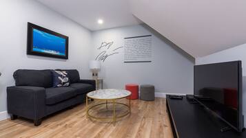 A modern living room with a dark sofa, a round coffee table, a flat-screen TV, and a framed picture on the wall.