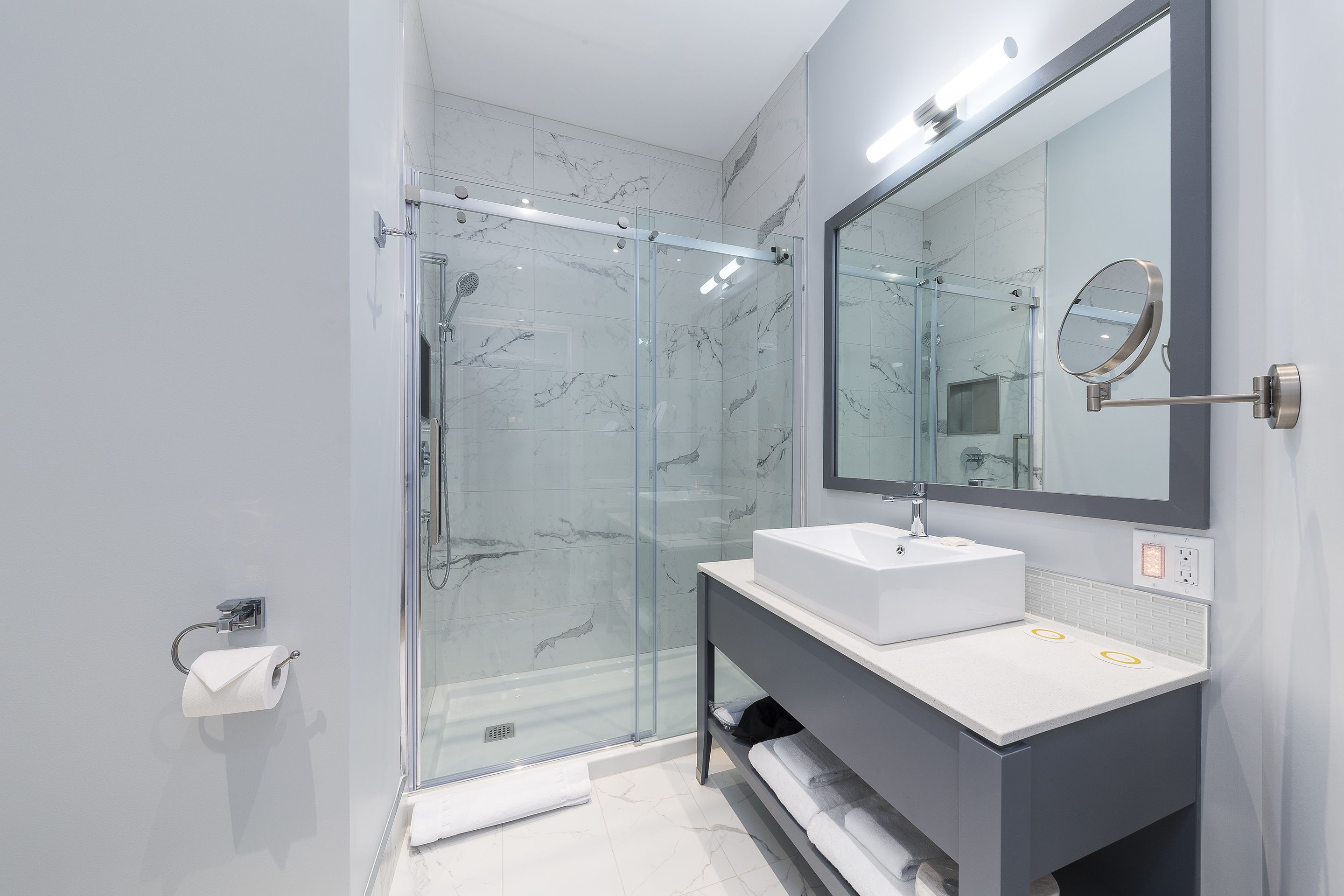 A modern bathroom with a glass-enclosed shower, a white sink, and a large mirror.