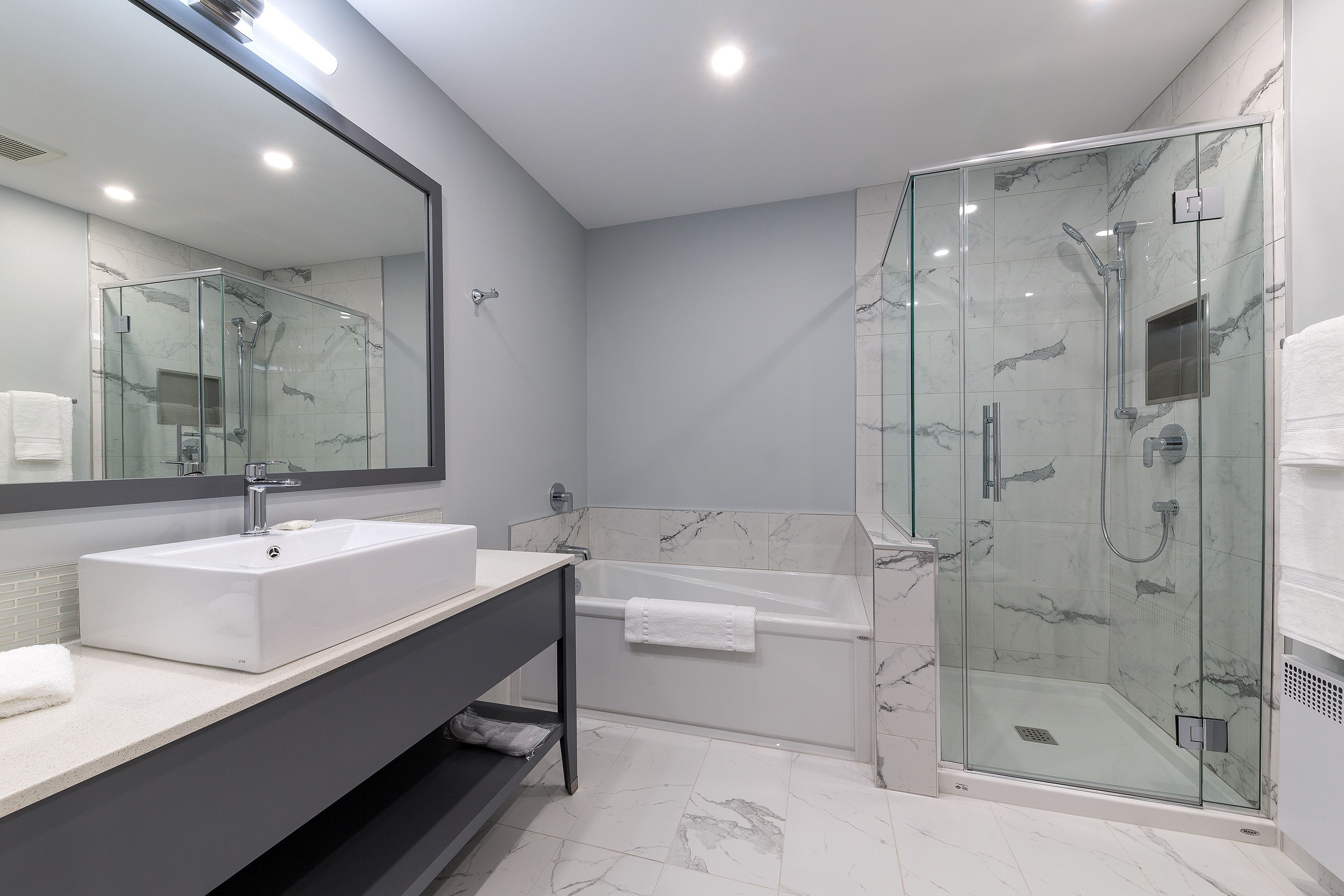 Un baño moderno con ducha envuelta en vidrio, una bañera independiente y un espejo grande sobre el lavamanos.