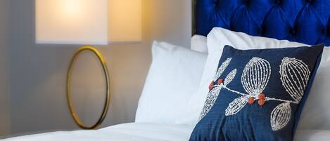 A neatly made bed with white linens, a blue upholstered headboard, and a decorative pillow with a floral pattern.