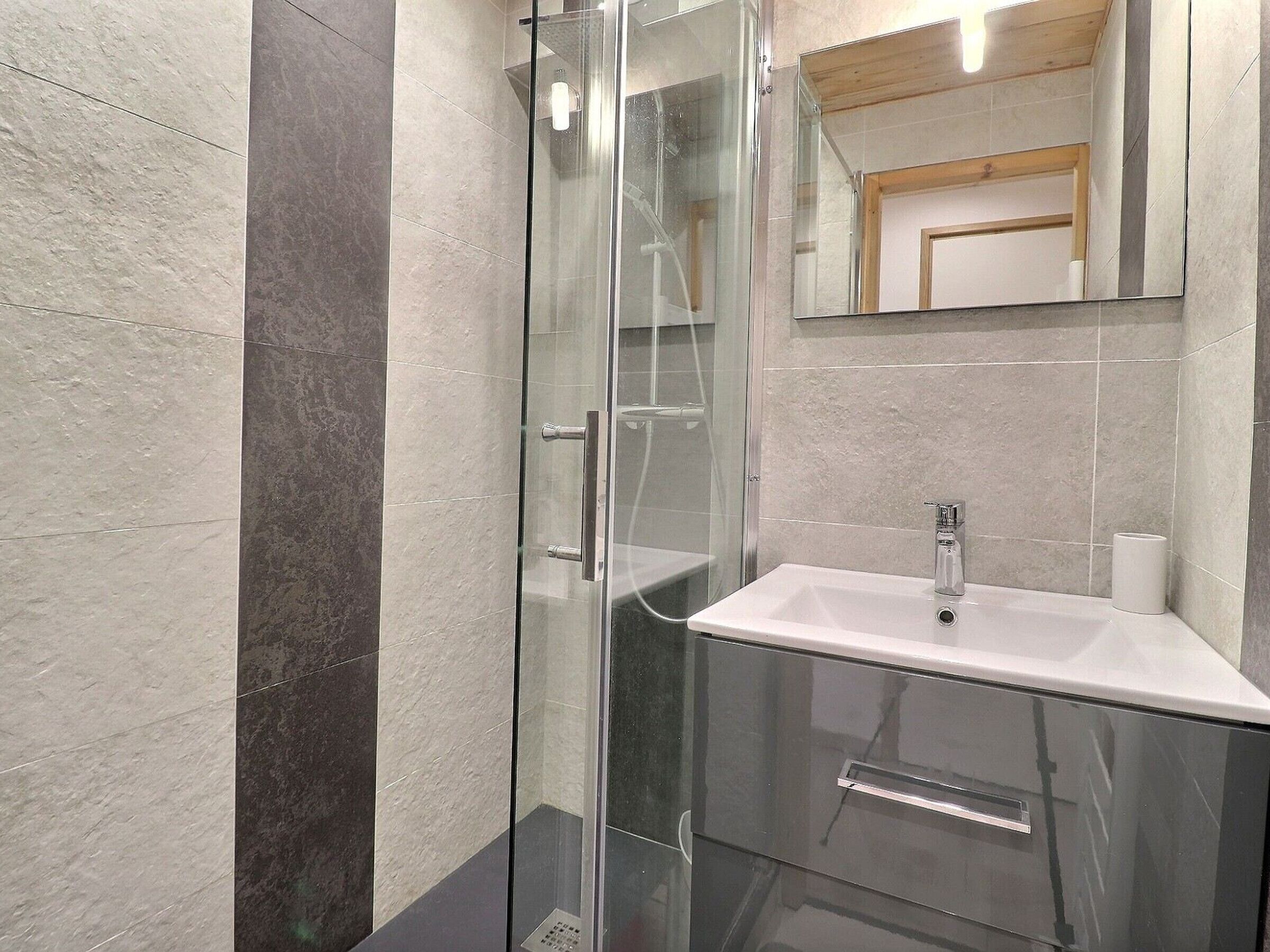 Ein modernes Badezimmer mit einer gläsernen Duschkabine, einem weißen Waschbecken und einem Spiegel darüber.