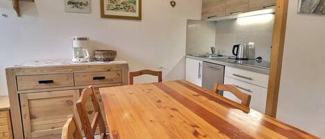 Une cuisine compacte avec une table et des chaises en bois, une machine à café et une bouilloire posées sur le plan de travail.
