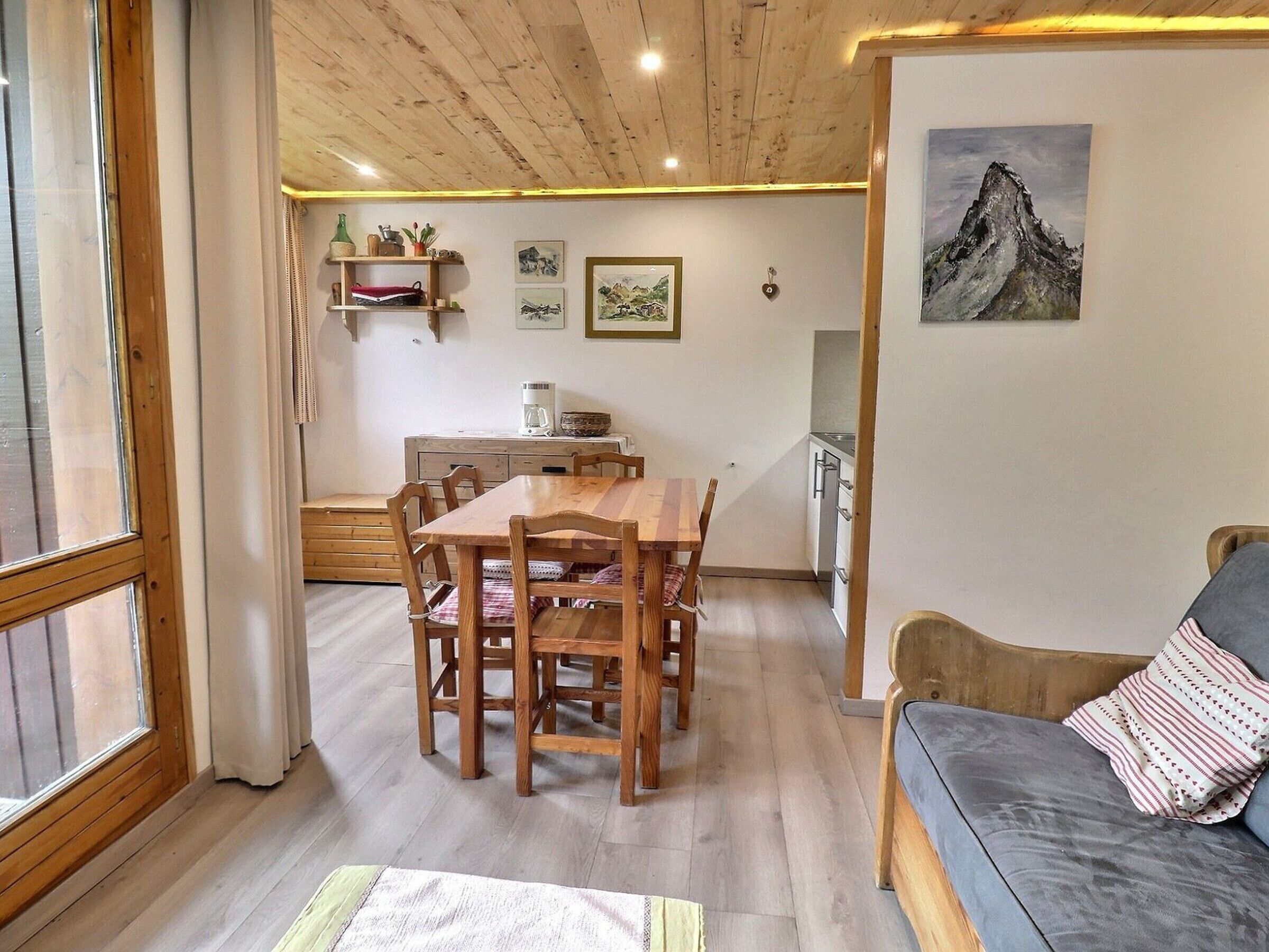 Ein gemütlicher Wohnbereich mit einem Holztisch, Stühlen, einer Couch und einer Küche im Hintergrund.