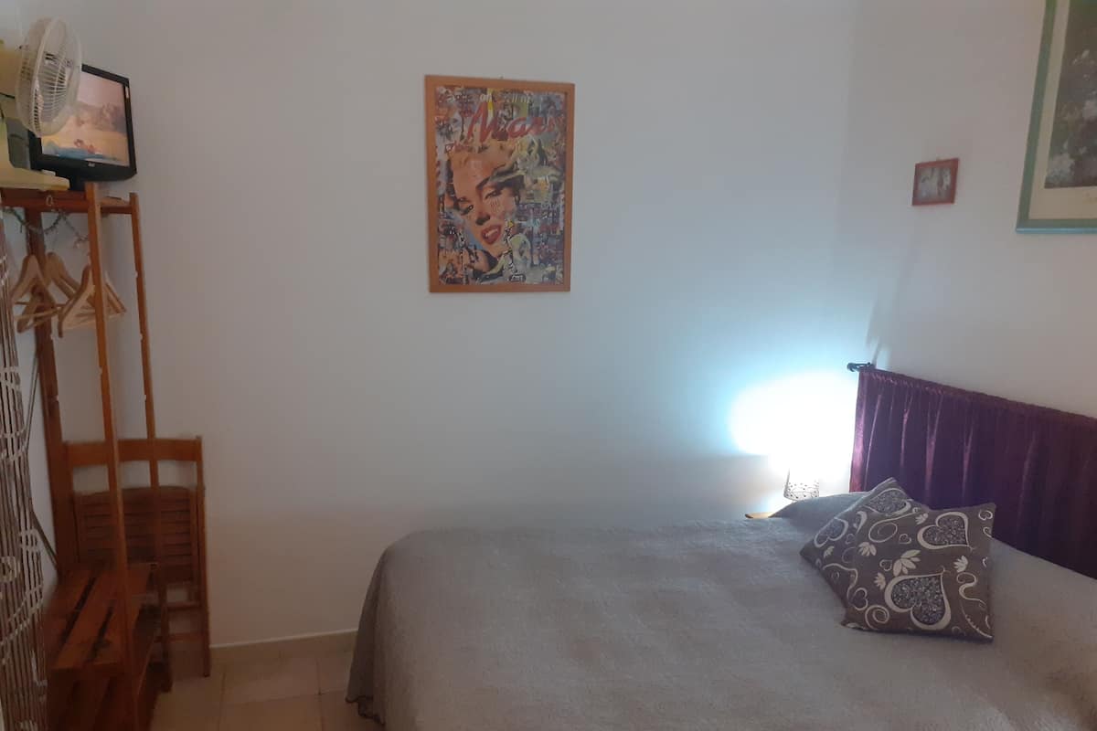 Ein Schlafzimmer mit einem Bett, einem Holzstuhl, einem an der Wand befestigten Fernseher und einem Gemälde.