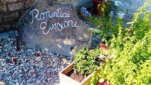 Une pancarte en pierre sur laquelle est inscrit « Romantica Evangeline Bed & Breakfast », entourée de plantes en pot et de petits galets.