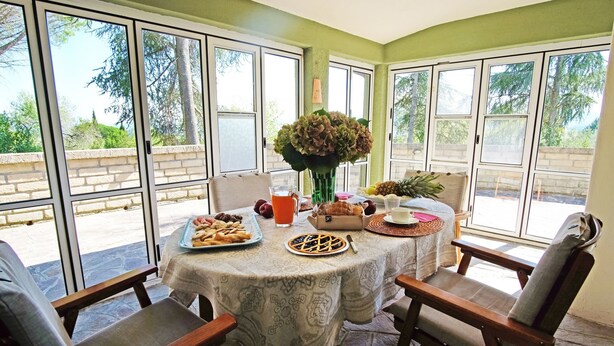 Un coin repas avec une table dressée pour deux personnes, un vase de fleurs et une variété d’aliments pour le petit-déjeuner.