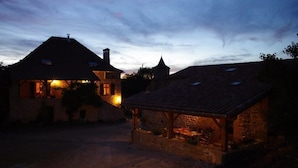Ein rustikales Gebäude mit Naturstein-Fassade und Ziegeldach, inklusive überdachter Außenbereich mit Sitzgelegenheiten.