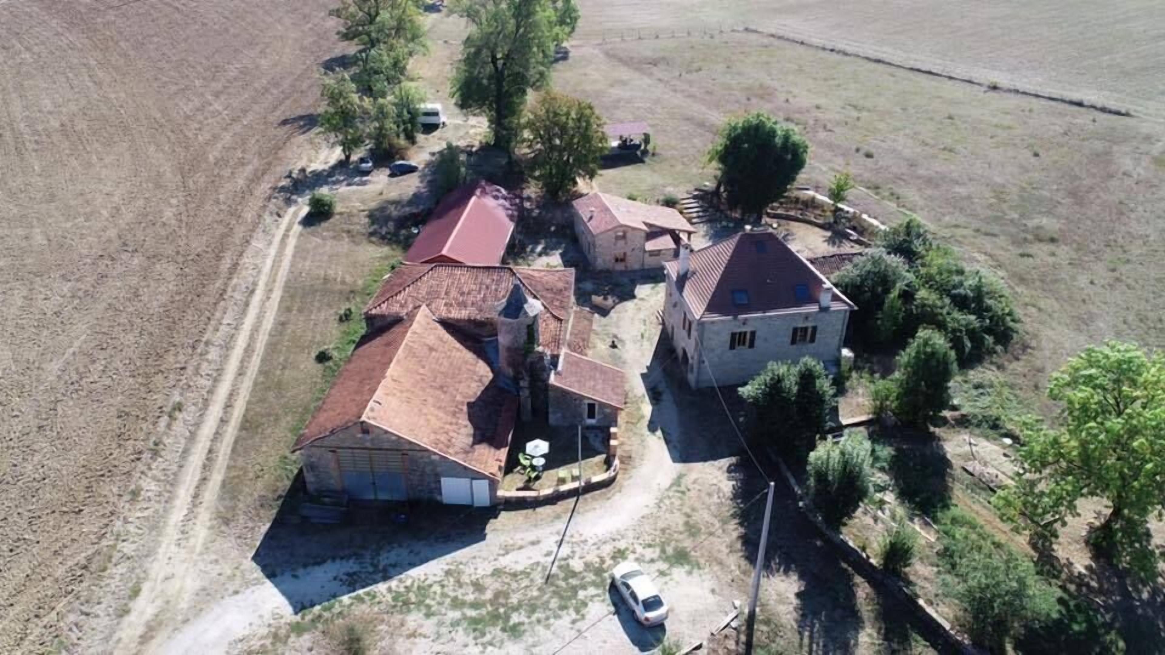 Vista aérea de una propiedad rural con varias construcciones, incluyendo una casa grande con techo rojo y estructuras más pequeñas. Se ven árboles y un camino de tierra.